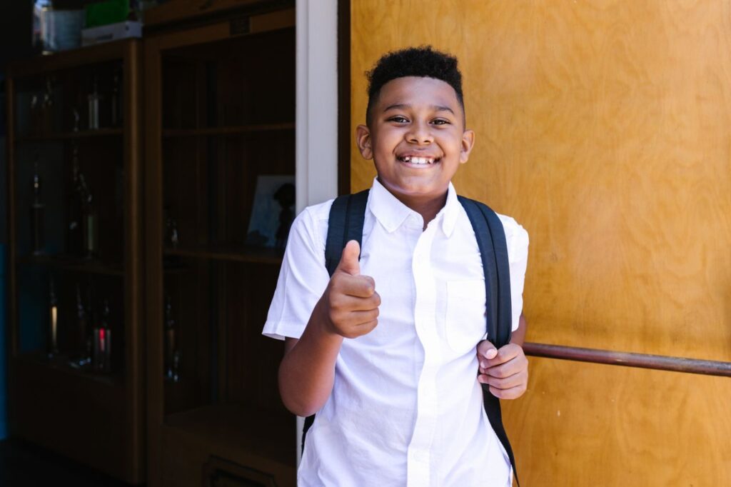 Crafting Captivating Headlines: Your awesome post title goes here Smiling student with backpack giving thumbs up, standing at school entrance.