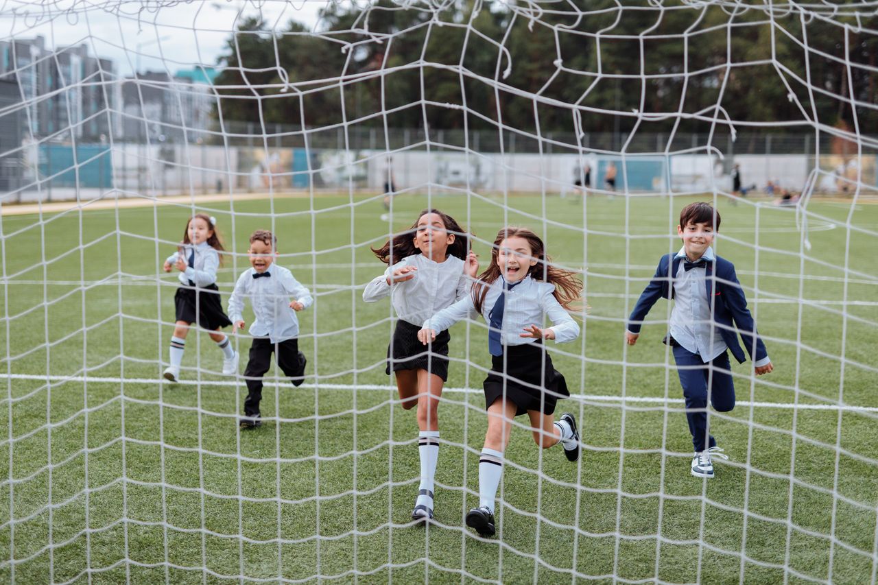 Group of children joyfully running towards the camera on a soccer field, showcasing a lively and playful moment.